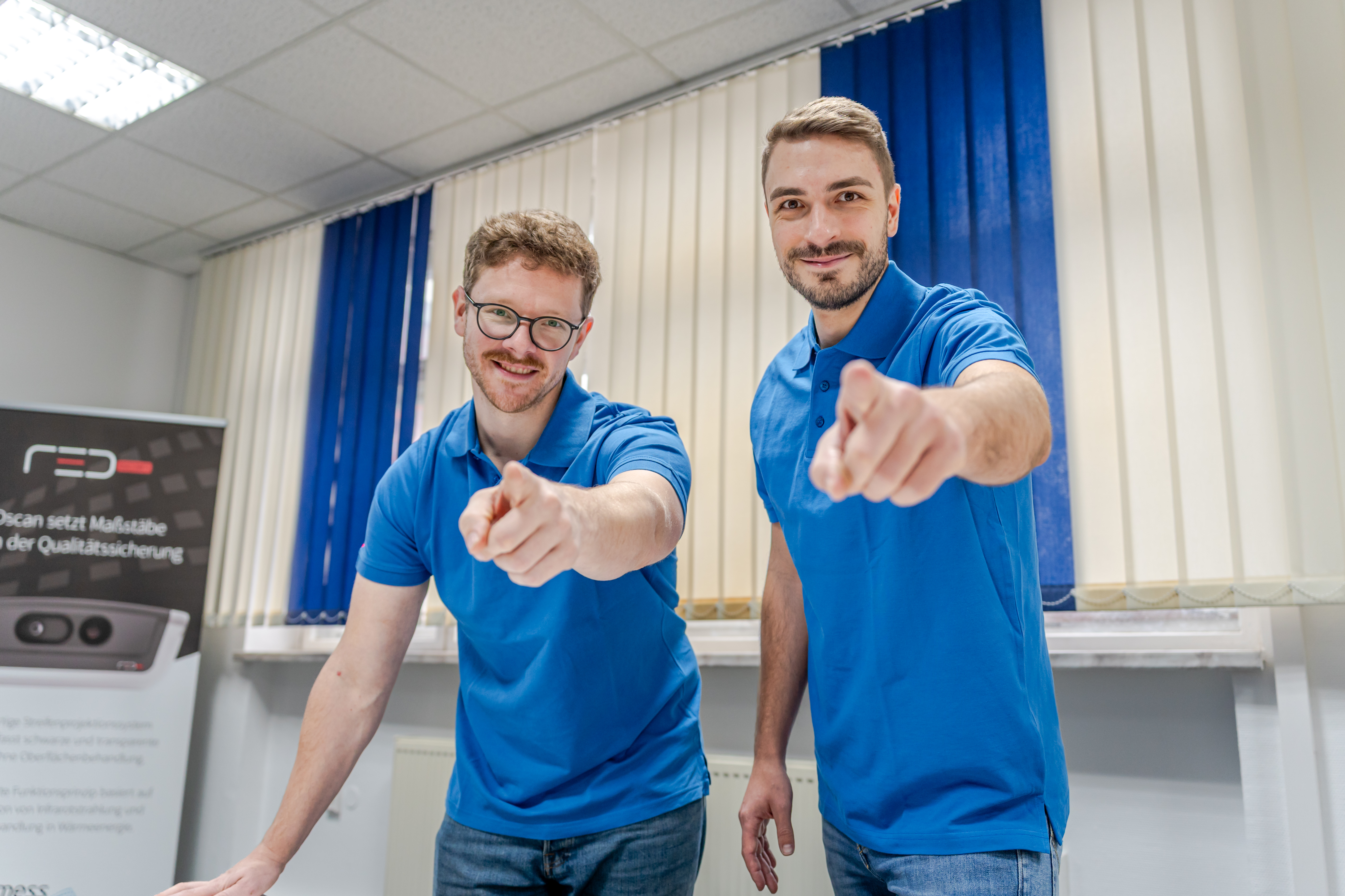 Zwei Aimess-Techniker zeigen in die Kamera